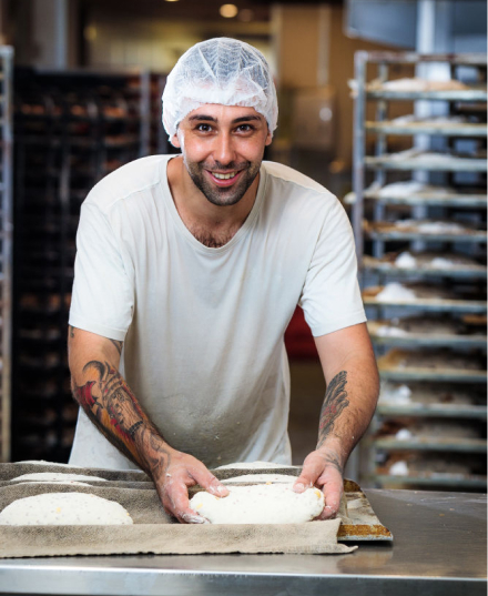 Professional lifestyle headshot of a male baker in a bakery shaping bread in Moore Park, Sydney, NSW.