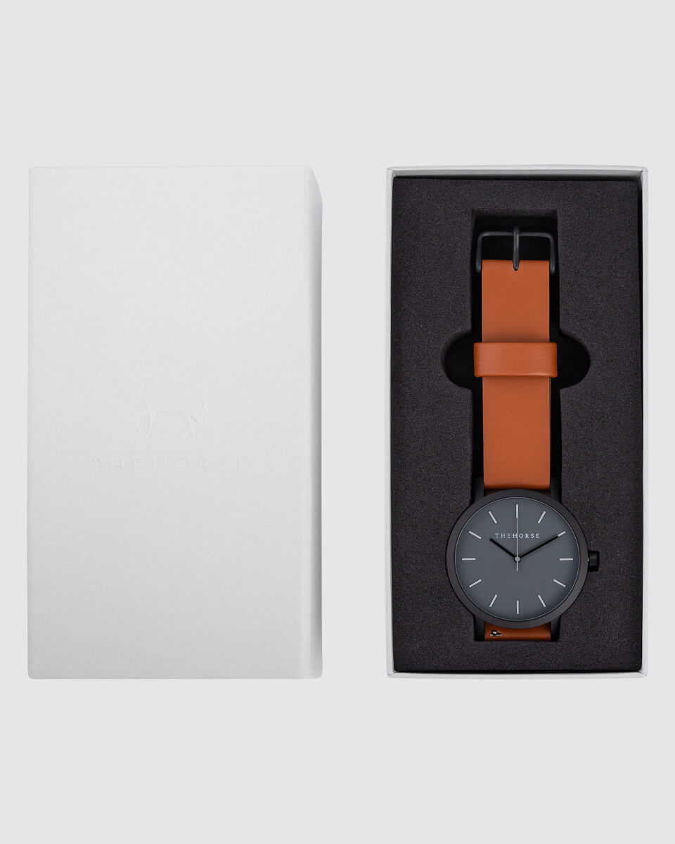 photo of a black watch with brown strap in a case