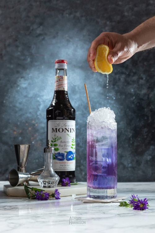 drinks and beverage photography in Sydney CDB. Hand squeezing lemon onto a cocktail with cocktail mixer in background.